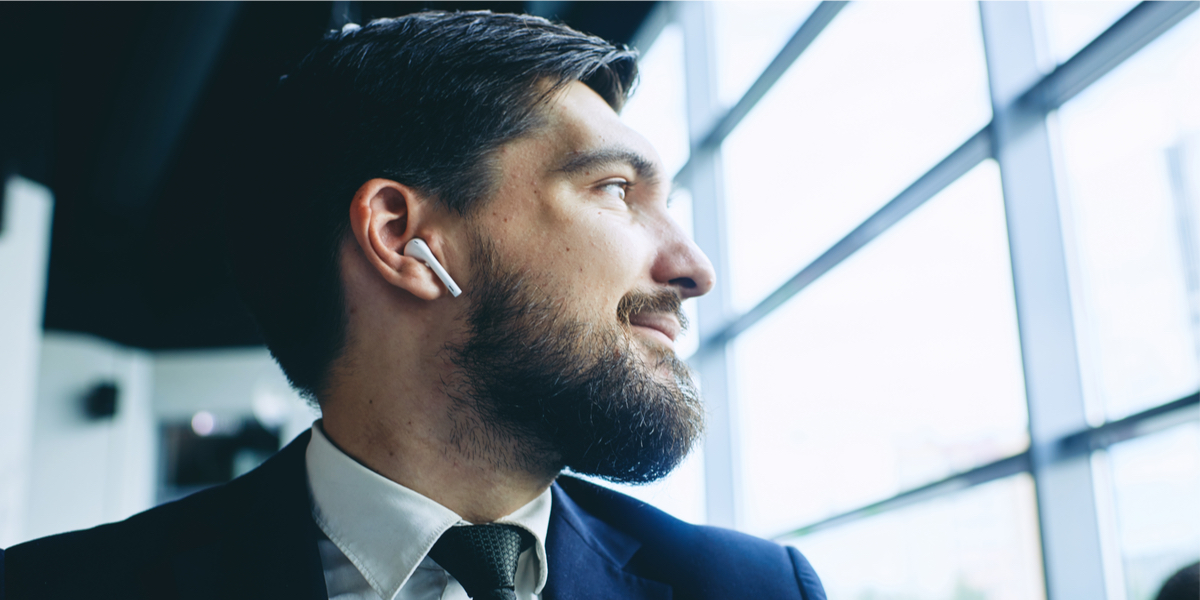 Bearded man in a suit looking through window with white wireless headphone in ear