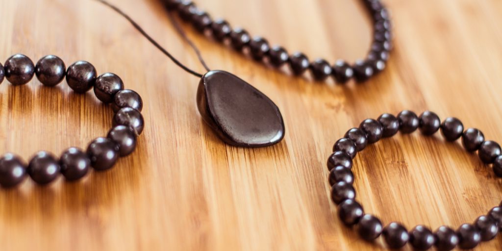 A black shungite stone necklace surrounded by three shungite bracelets on a wooden table