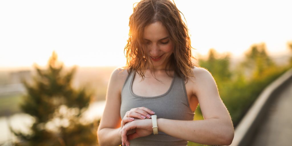 Woman standing outdoors smiling looking down at Fitbit activity tracker on her wrist