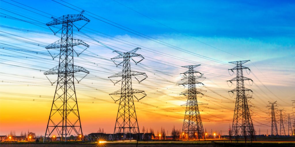 Sunset with housing building and tree on the bottom and large, high voltage power lines as the main focus