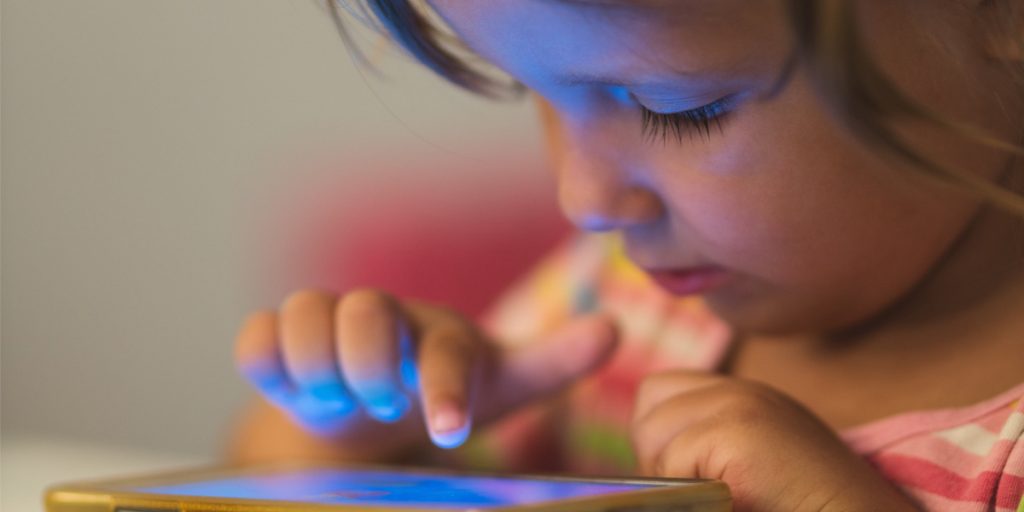 Young child operating a cell phone with one hand while looking over it