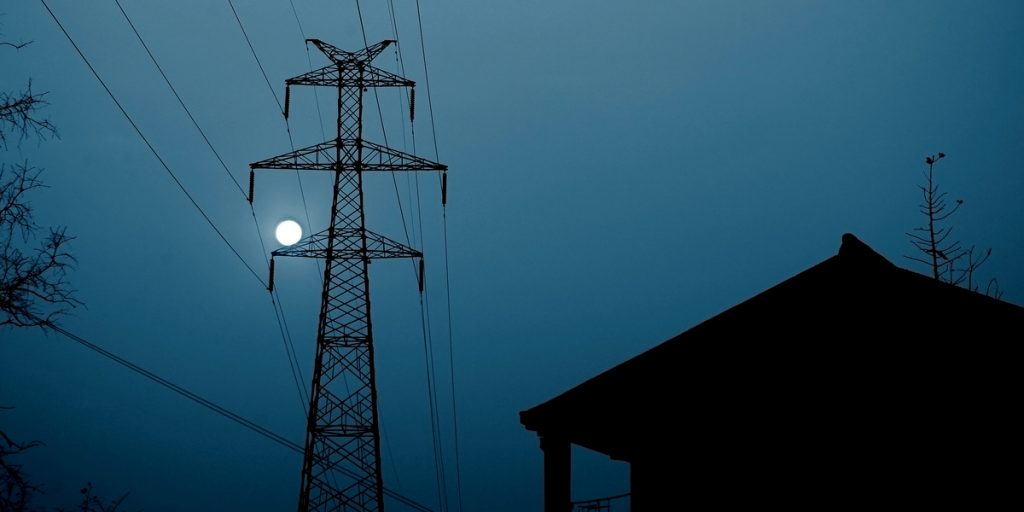 Nighttime looking up at a power line with the moon in the background and the side of a house in the foreground