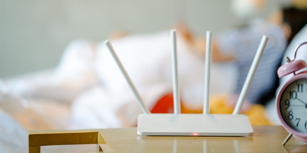 White wireless router on a table in the foreground with a woman in bed in the background