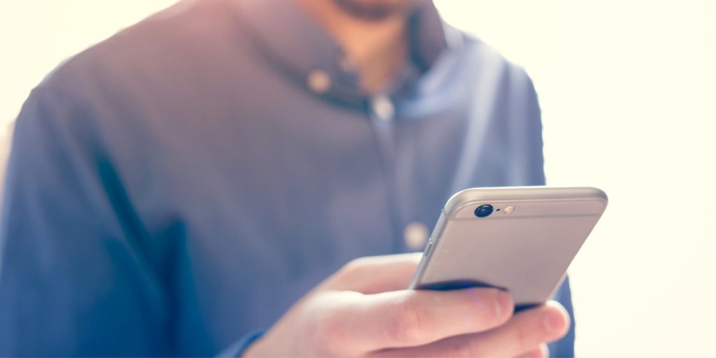 Man wearing a blue shirt holding a silver iPhone