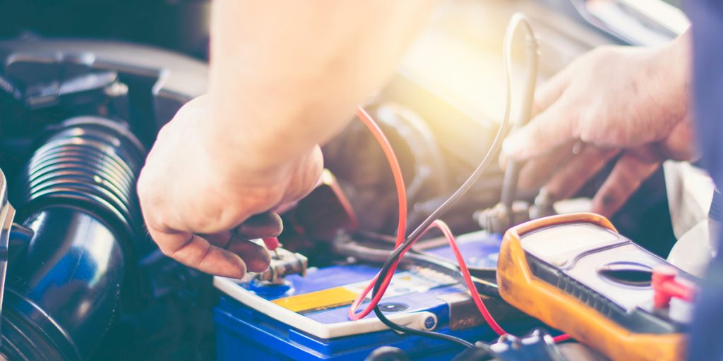Car battery with man using a multimeter to check the voltage