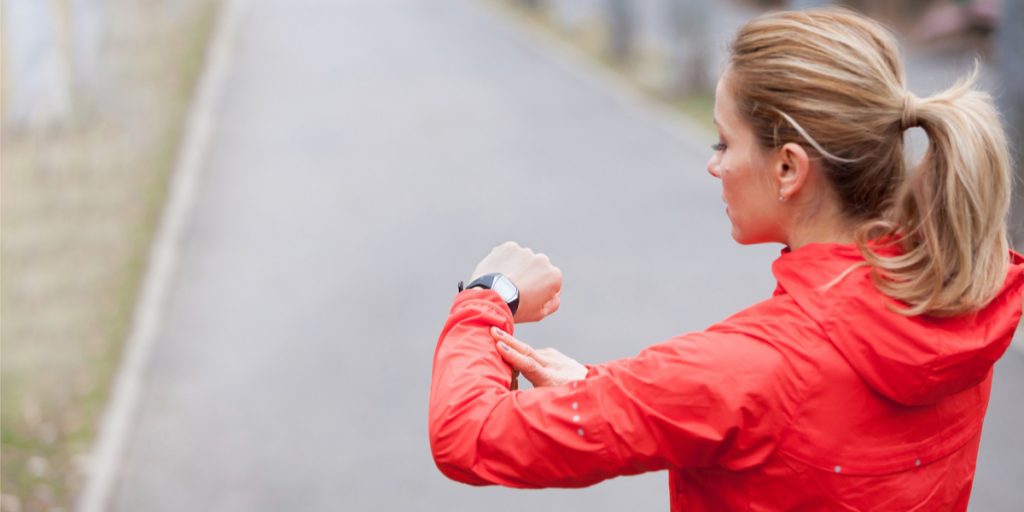 Woman wearing red jacket outside for a walk looking at fitness tracker watch on her arm