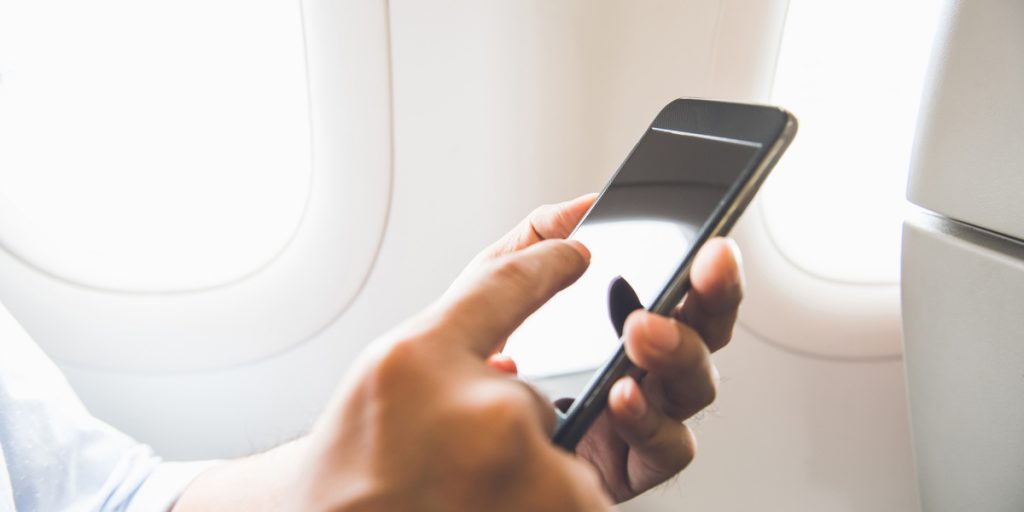 Person sitting on a plane with a cell phone turning it to Airplane Mode