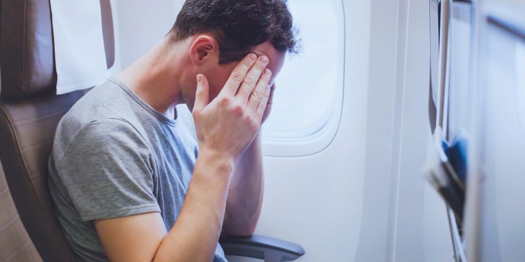 Man sitting on an airplane rubbing his forehead like he has a headache
