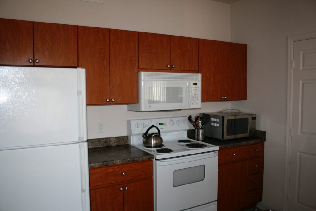 Kitchen with white refrigerator, white oven, and white microwave with wood cabinets and dark counter tops and a second microwave sitting on the counter