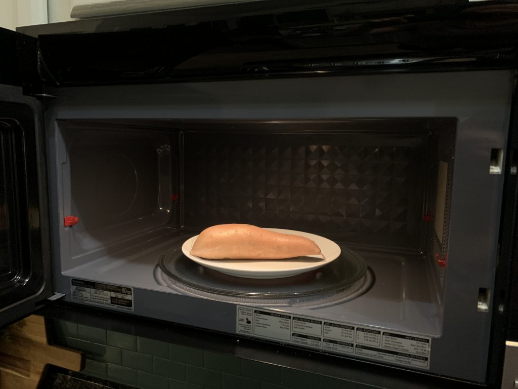 Close up of microwave oven with door open and a sweet potato inside on top of a white plate